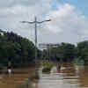 A postman wades through flooded road in Yemalur Main Road in Bengaluru on Tuesday.