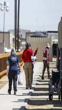 Disaster medical assistance team workers walk in-between housing units at temp holding facility for migrants.