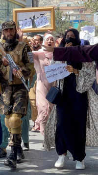 Taliban forces walk in front of Afghan demonstrators