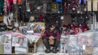 ​A shopkeeper warms his hands around a <i class="tbold">kangri</i>