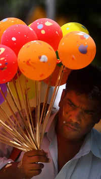 A toy vendor cover his face from the heat by balloons.