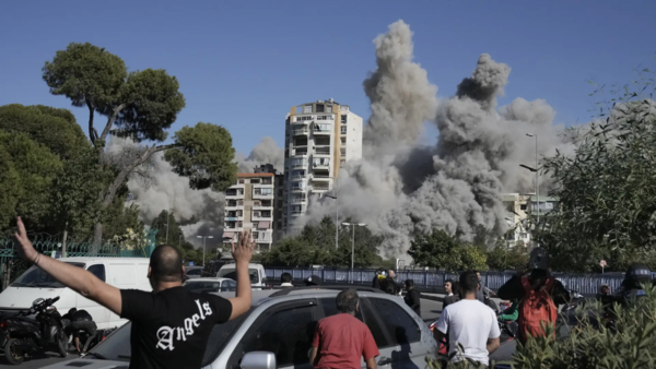 People watch a building collapse after being hit by an Israeli airstrike (AP)