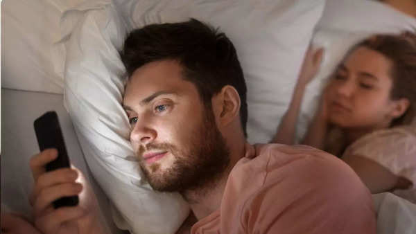 Man is using phone while woman is sleeping