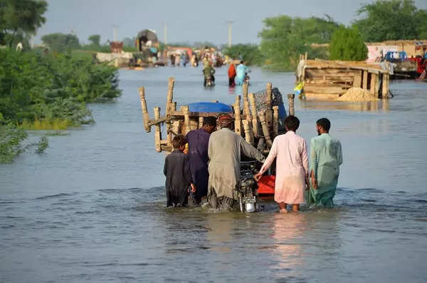 Men walk along a flooded road with their belongings, following rains and floods during the monsoon season in Sohbatpur.