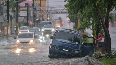People abandon a car on an impassable street flooded by rains caused by Tropical Storm Melissa (Image credits: AP) Melissa strengthens to a Category 5 hurricane as it nears Jamaica