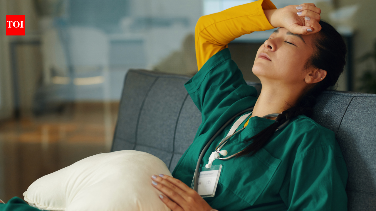 A tired person sitting by a window, holding their head with one hand