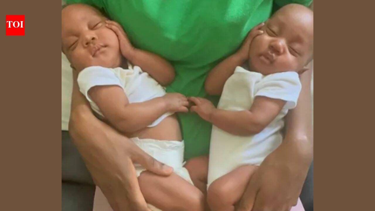 Two babies in white outfits being held by an adult.