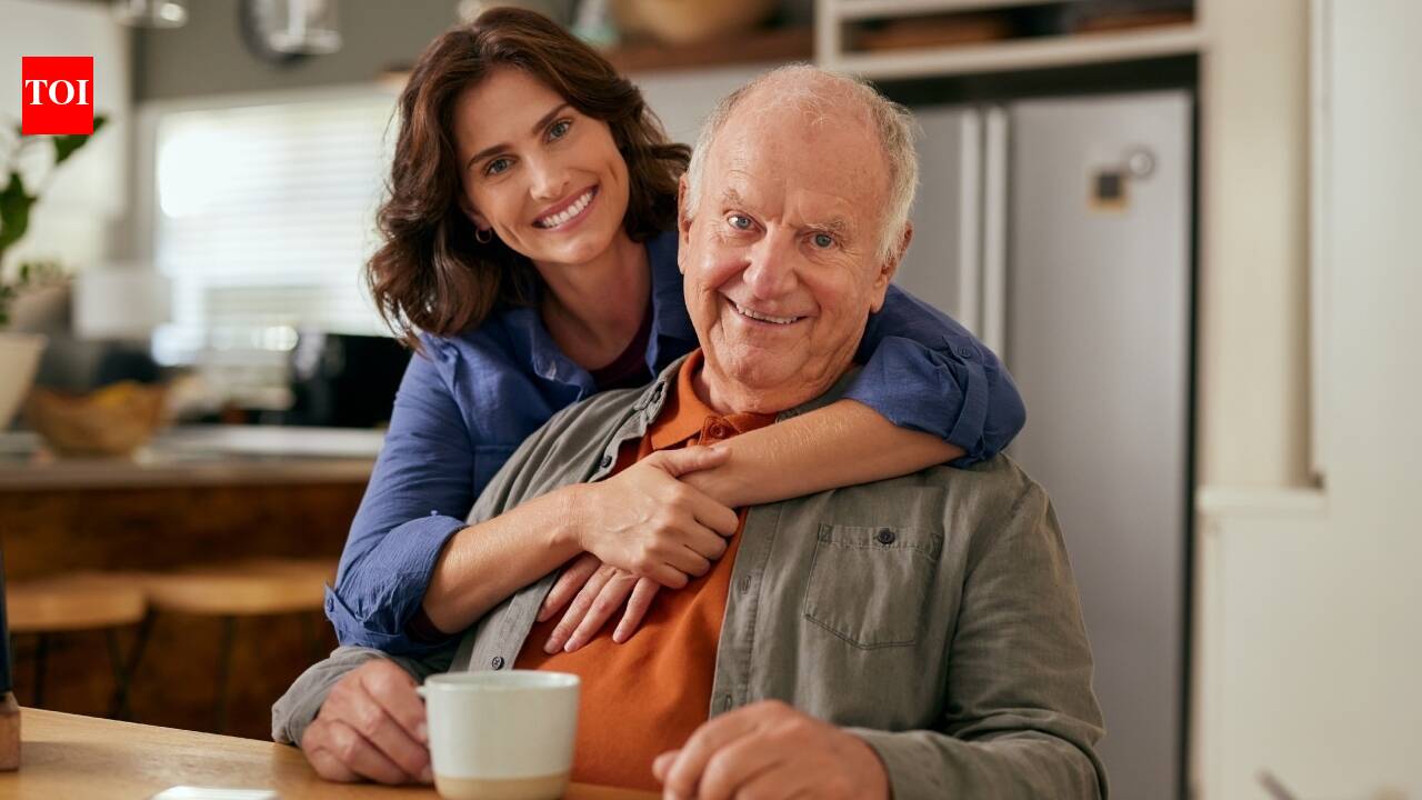 A smiling woman embraces an older man in a kitchen.
