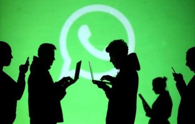 Silhouettes of laptop and mobile device users are seen next to a screen projection of Whatsapp logo in this picture illustration taken March 28, 2018. REUTERS/Dado Ruvic
