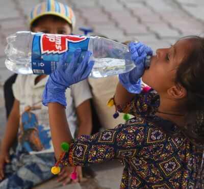 A girl sits on a pavement and drinks water outside the New Delhi Railway Station on a hot day in Delhi on Friday.