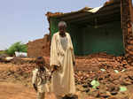 A man walks with his son outside a damaged building in Al-Managil locality during floods in Jazeera State