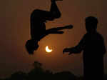 The partial solar eclipse is framed by youngsters jumping on a trampoline in the...