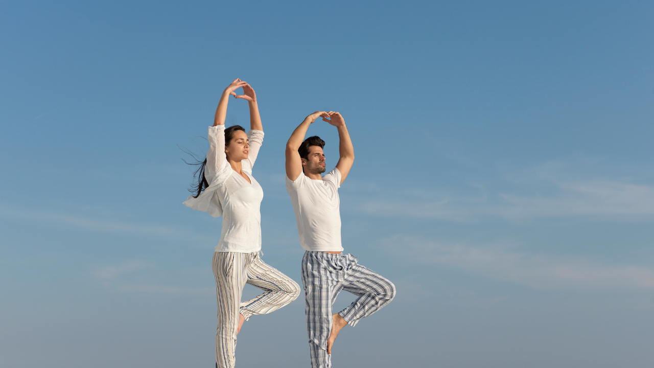 Couple of young smiling sporty people practicing yoga lesson with partner,  man and woman standing in Vrksasana exercise, Tree pose, working out,  indoor full length, studio. Wellbeing, wellness concept Stock Photo |