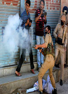 A police officer fires tear gas shell towards stone-pelters